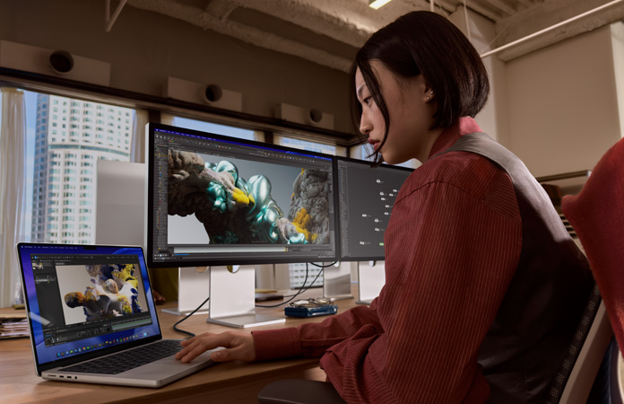 一個人在辦公室環境中工作，MacBook Pro 連接著 Studio Display XDR