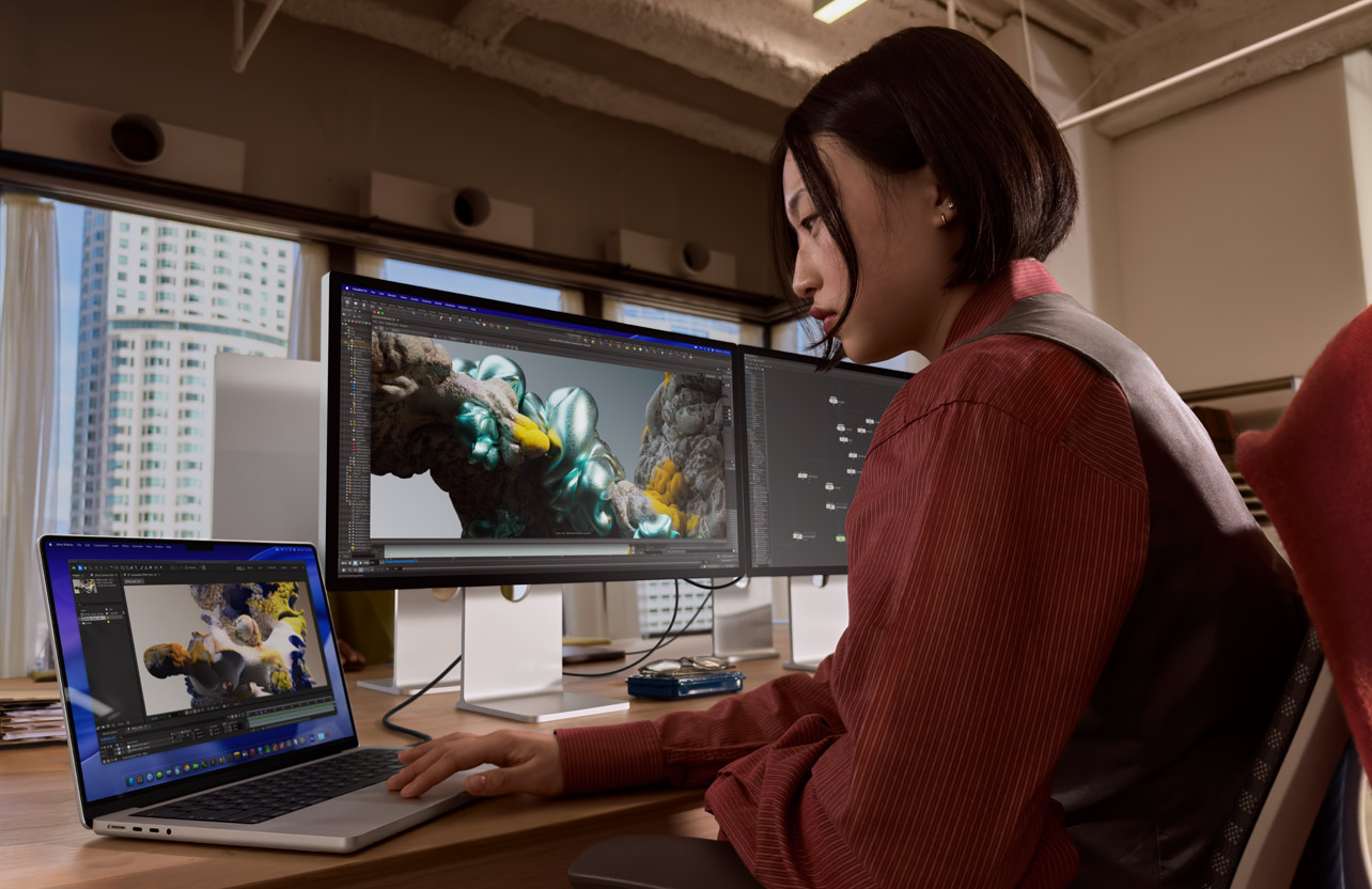 A person working in an office setting with MacBook Pro connected to Studio Display XDR