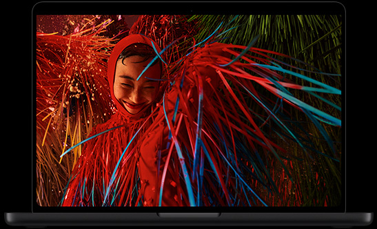 MacBook Pro with PROLED XDR Display, space black color, open, display shows a photo of a smiling person in a surreal red outfit with feathery details