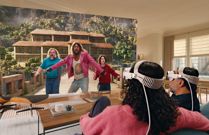 Apple Vision Proを装着した2人がソファに並んで座り、部屋いっぱいに広がるスクリーンに映し出される「マインクラフト／ザ・ムービー」を観ている