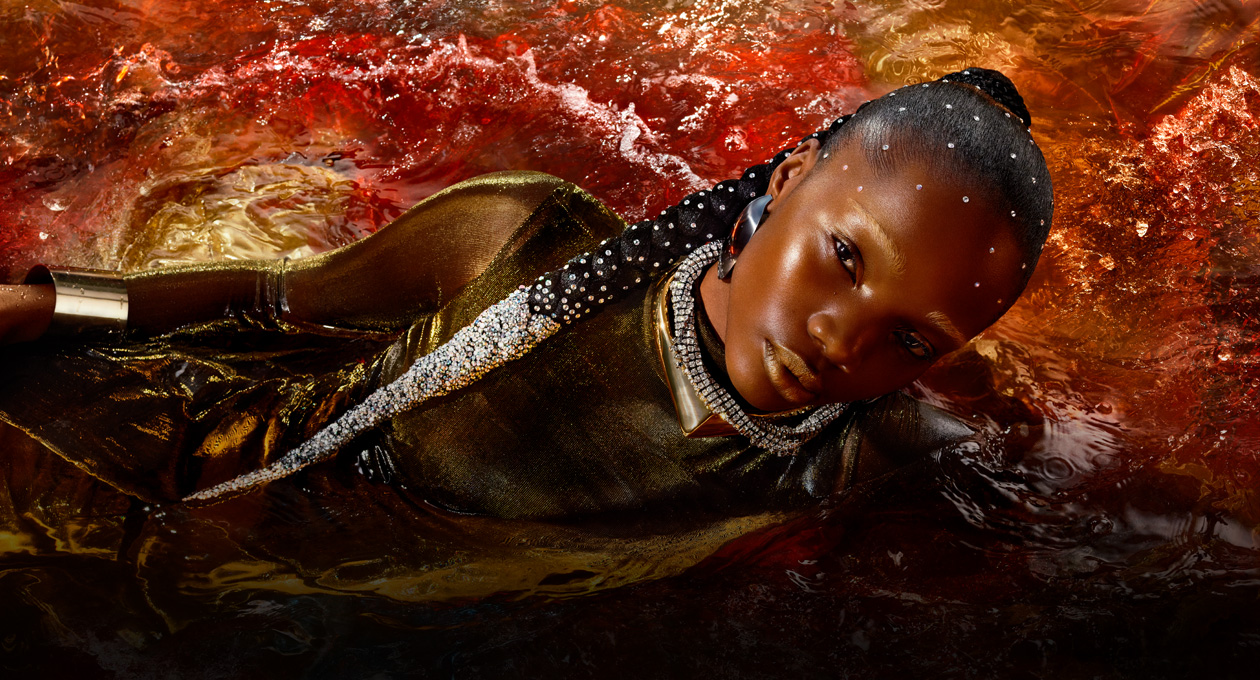 Een model in een goudkleurige jurk dat op haar zij in een plas roodgekleurd water ligt om de helderheid, het contrast en de brede kleurweergave van Studio Display XDR te laten zien
