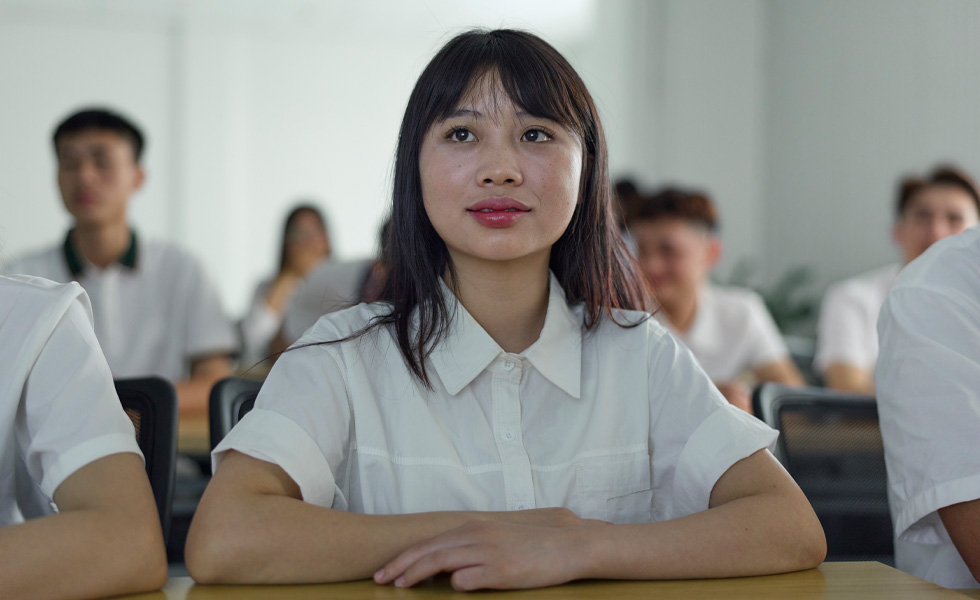 Six people wearing white button-up short sleeves sit focused on the front of the classroom