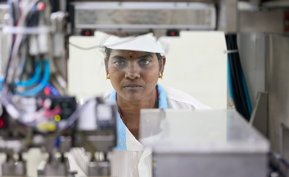 A robotics employee holds a work device as they peer at a robotics machine