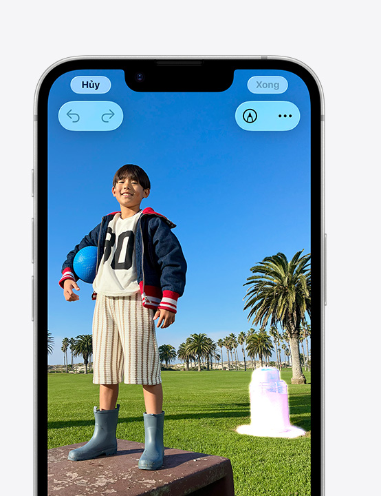 iPhone screen, photo of person smiling on a park ledge, showing how to remove a trash can in the background with the Clean Up tool