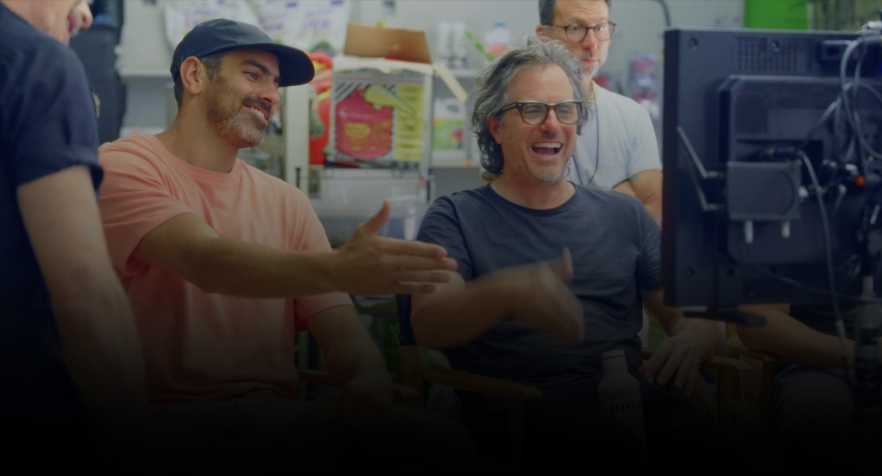 2人の男性映像制作者が椅子に座り、プロジェクタースクリーンを見ながらジェスチャーをしている画像