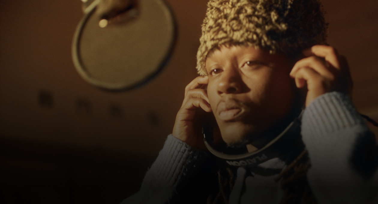 音楽スタジオで録音用マイクの前に立ち、ヘッドフォンで聴いているKiddo K氏の写真